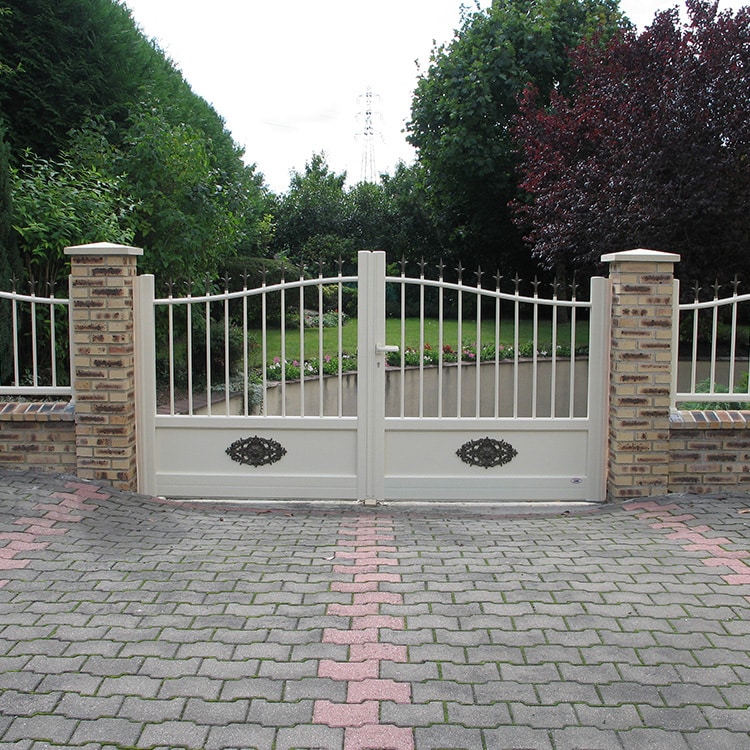 Portail battant aluminium beige : style classique et élégance. Portail battant beige en aluminium sur mesure, style classique semi-plein, avec décorations noires. Piliers en brique claire. Allée pavée vers le jardin.