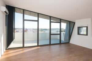 Appartement moderne vide avec parquet et grande baie vitrée ouvrant sur une terrasse avec vue dégagée.