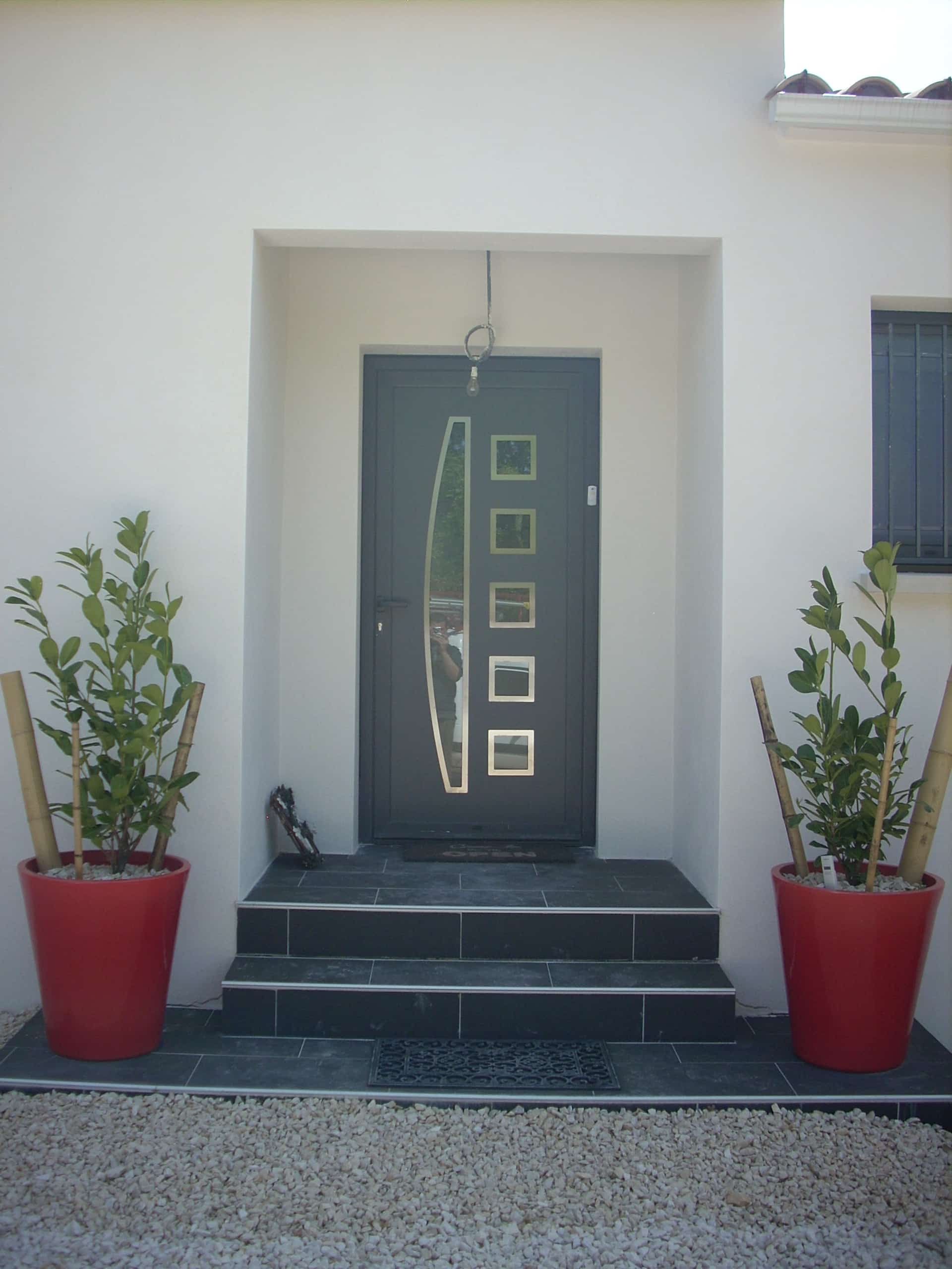 Porte d'entrée moderne anthracite avec vitres et grands pots rouges décoratifs sur un perron en carrelage sombre.