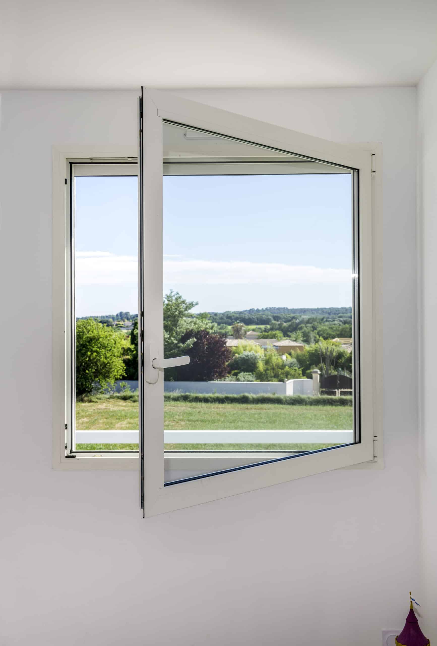 Fenêtre en PVC blanc ouverte en oscillo-battant offrant une vue dégagée sur un jardin ensoleillé et verdoyant.