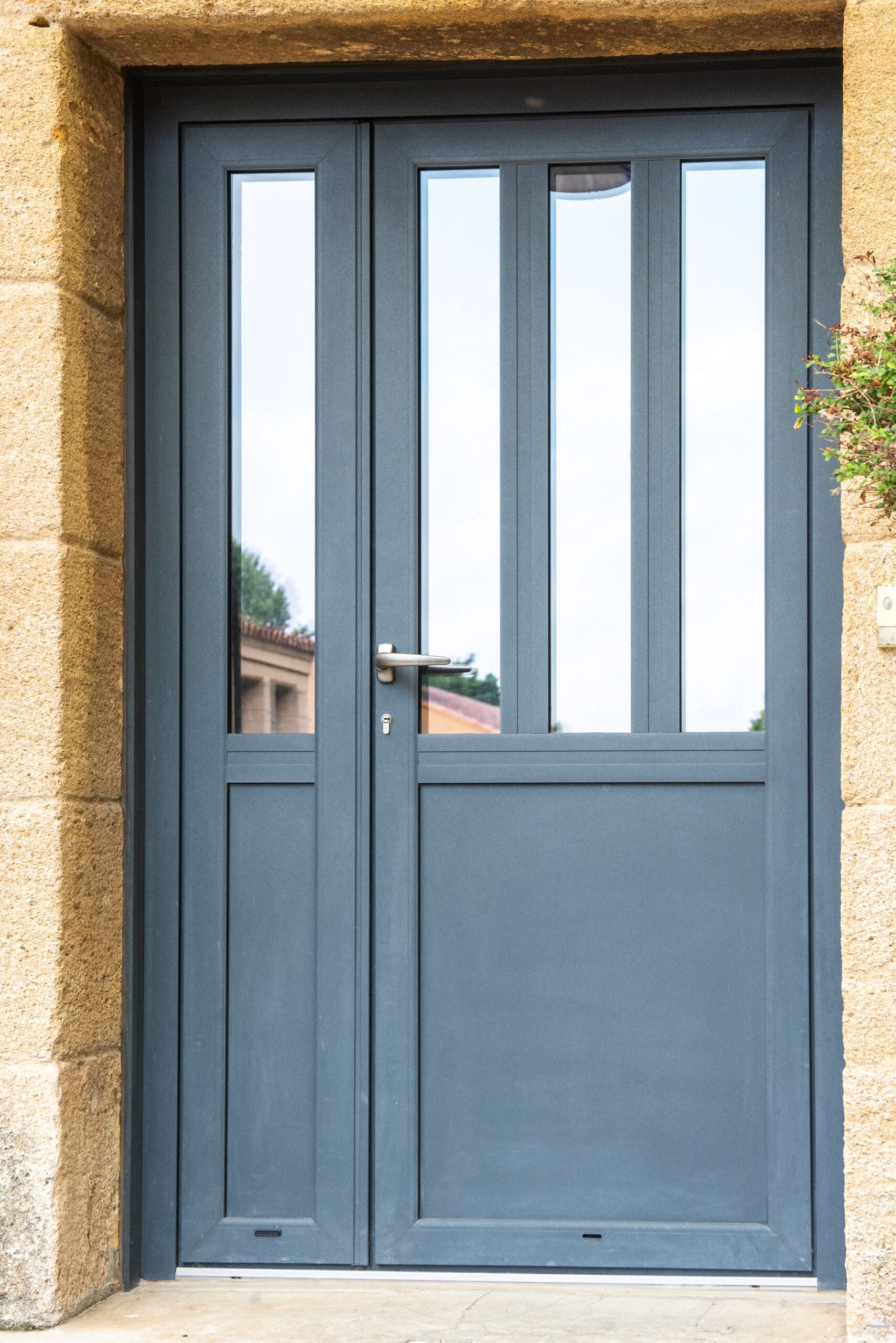 Porte d'entrée gris anthracite moderne avec vitrage vertical dans un encadrement en pierre.