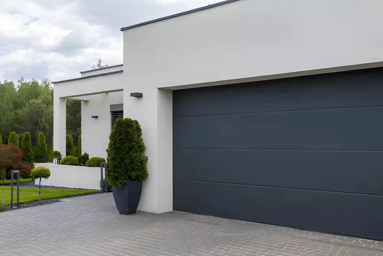 Porte de garage sectionnelle grise sur façade de maison blanche moderne et allée pavée.